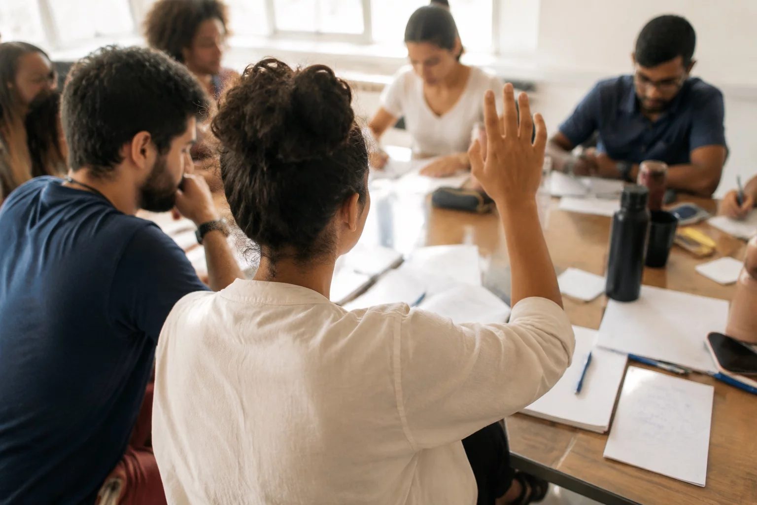 Estudante levantando a mão em uma mesa de seminário coberta de anotações