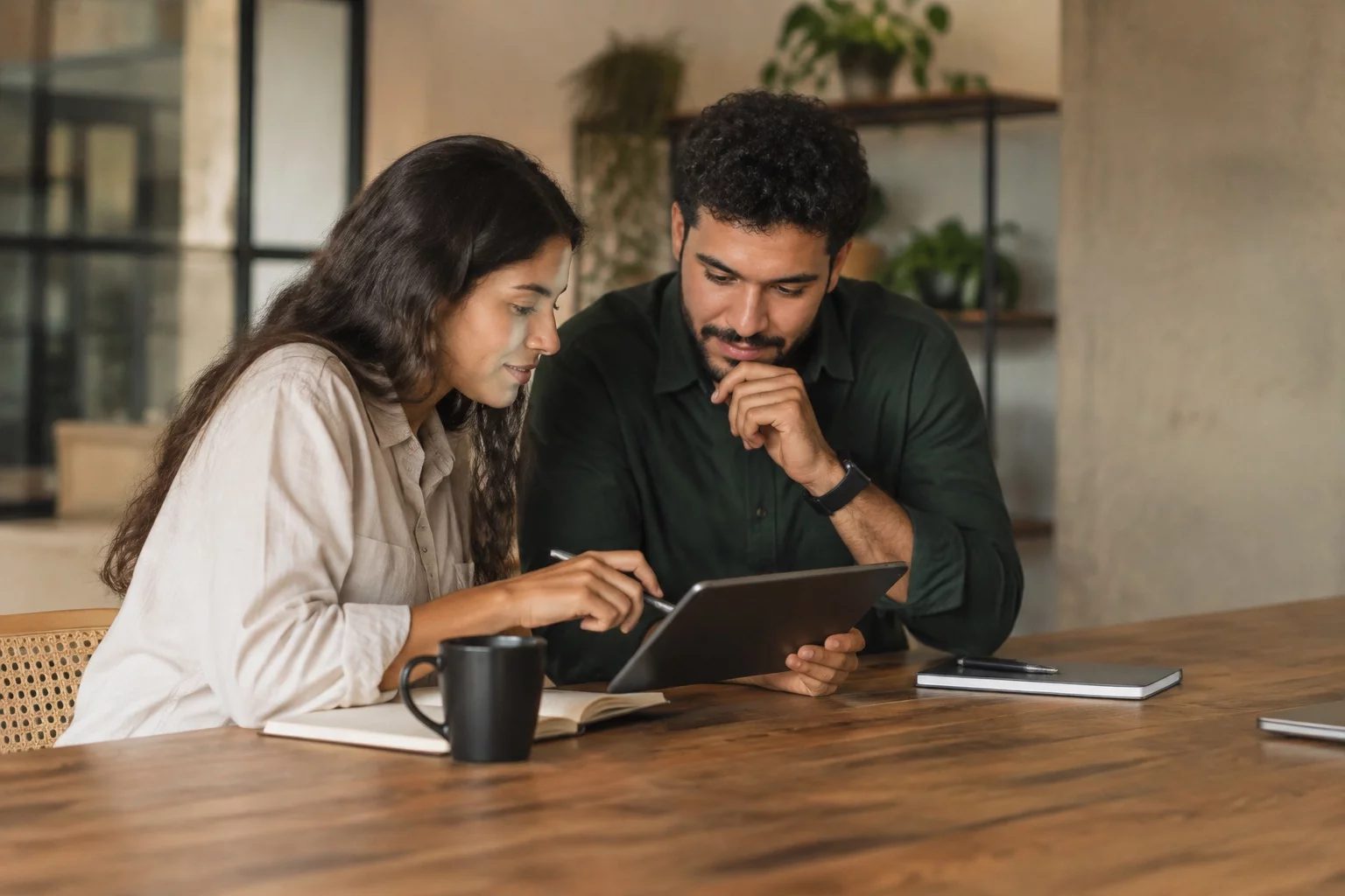 Duas pessoas revisando anotações em um tablet sobre uma mesa de madeira